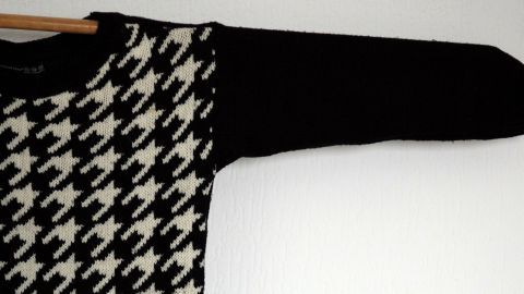 Ein gestreifter Wollpulli hängt an einem Kleiderbügel, bereit zum Trocknen in einem hellen Raum.