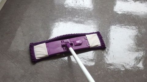 Ein Wischmopp reinigt glänzendes Laminat auf einem glatten Boden in einem hellen Raum mit Fensterlicht.