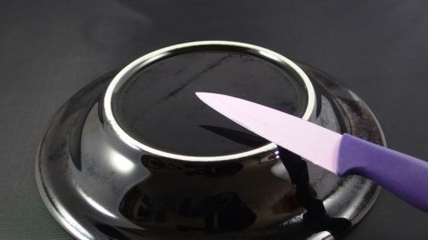 Ein schwarzer Teller wird verwendet, um ein Messer mithilfe seiner Unterseite zu schärfen. Der Teller steht auf einer dunklen Oberfläche.