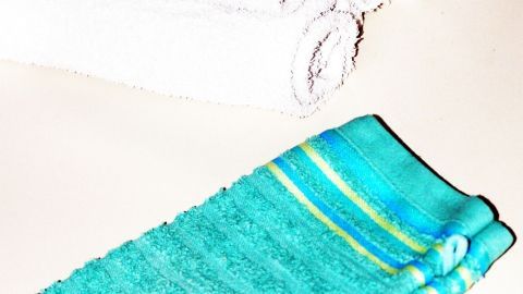 Ein blauer Waschlappen liegt neben einem Stapel von weißen Handtüchern, was auf das Waschen von Textilien hinweist.