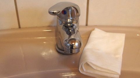Mikrofasertücher sind einfach super für Fenster, Spiegel, Fliesen, Waschbecken, Badewanne, Spüle u.v.m. Man benötigt keine Reinigungsmittel mehr. Ein verkalkter Wasserhahn steht auf einem Waschbecken, daneben liegt ein Reinigungstuch für die Pflege.