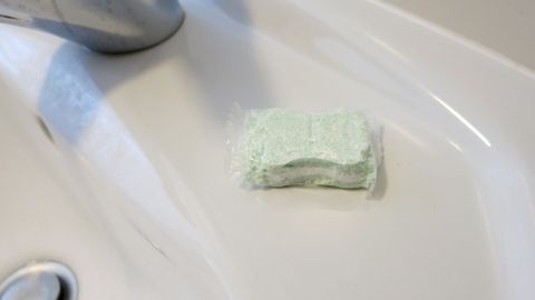 Eine weiße Keramikspüle wird mit einem grünen Schwamm gereinigt, der auf der glatten Oberfläche liegt.