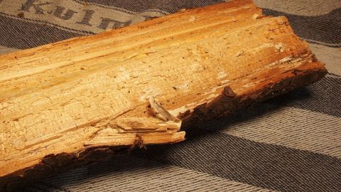 Ein Stück Holz liegt auf einem gestreiften Tuch, umgeben von unscharfem Hintergrund, bereit zur Behandlung mit Milch, um Harz zu entfernen.