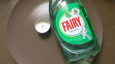 Eine grüne Spülmittelflasche liegt neben einer kleinen Kerze auf einem braunen Teller, ideal für eine Flohfalle.