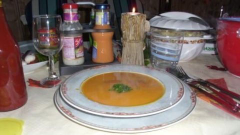 Eine cremige Kürbissuppe in einer Schüssel wird auf einem gedeckten Tisch serviert, umgeben von verschiedenen Gewürzen und Geschirr.