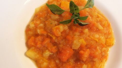 Eine bunte Zucchini-Möhren-Kartoffel-Suppe auf einem weißen Teller, umgeben von frischem Basilikum, appetitlich angerichtet.