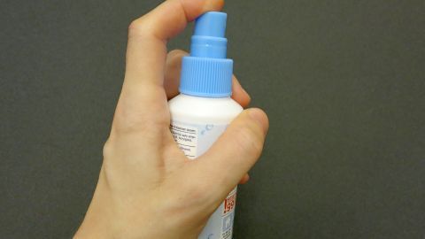 Eine Hand hält eine Sprühflasche, die anscheinend zum Schutz vor Pickeln nach der Intimrasur verwendet wird.