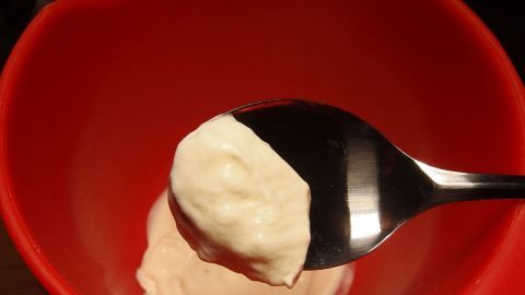 Sahne lässt sich schneller und besser schlagen, wenn man Schüssel und Schläger vorher im Eisfach kühlt. Ein Löffel mit geschlagener Sahne wird in eine rote Schüssel gehalten, um die Zubereitung zu zeigen.