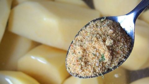 Ein Löffel mit einer salzfreien Gewürzmischung schwebt über rohen, geschälten Kartoffeln in einem Topf.