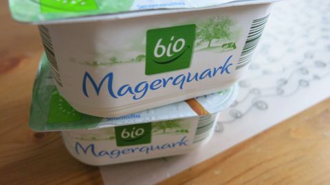 Gute und günstige Gesichtsmaske ganz ohne Chemie selber machen, mit 40%igem Quark aus dem Kühlregal. Zwei Becher von Magerquark stehen auf einem Holztisch, bereit zur Verwendung für eine chemiefreie Gesichtsmaske.