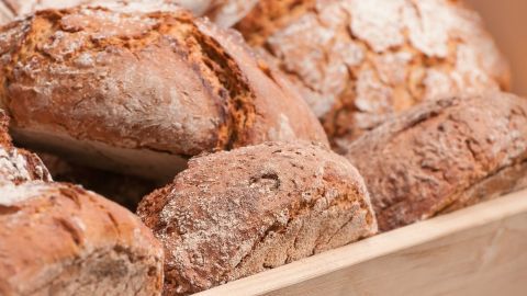 Eine Auswahl goldbrauner Weizenmischbrote liegt rustikal in einem Holzkasten, frisch gebacken und duftend.