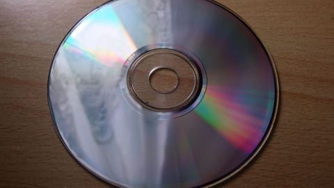 Unterseite einer zerkratzten CD mit Autopolitur und Polierwatte polieren. Ein glänzender CD-Rohling liegt auf einer Holzoberfläche, das Licht reflektiert sanft die Kratzer. Perfect für Autopolitur!