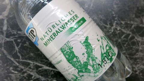 Verwöhne dein Haar mit einem erfrischenden Mineralwasser-Spülungstipp. Das kohlensäurehaltige Wasser sorgt für Glanz und entfernt Rückstände – alles, was du brauchst, ist diese einfache Flasche Mineralwasser. Dein Haar wird es dir danken! Flasche mit "Tip Natürliches Mineralwasser medium" liegt auf einer dunklen Marmoroberfläche. Text: "Mit Kohlensäure".