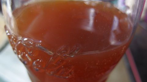 Ein Glas gefüllt mit einer sprudelnden Mischung aus Cola und Apfelsaft steht auf einem Tisch.