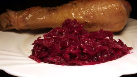 Auf einem weißen Teller liegt eine Portion Rotkohl aus dem Glas, appetitlich neben einem goldbraun gebratenen Hähnchenschenkel.