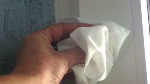 Ein Handgreift mit einem Tuch reinigt strahlend weiße Kunststoff-Fensterrahmen in einem hellen Innenraum.