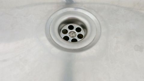 Ein metallener Ausguss mit Löchern im Abfluss, umgeben von einer glatten, silbernen Oberfläche, wirkt sauber und unbenutzt.
