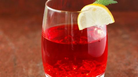 Ein Glas gefüllt mit rotem Wodka, garniert mit einer Zitronenscheibe und Minze, steht auf einem rustikalen Tisch.