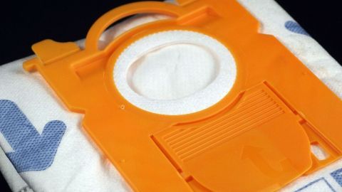 Ein orangefarbener Staubsaugerbeutel mit Verschluss liegt auf einem weißen Tuch, bereit zum Wechseln, um Gerüche zu vermeiden.
