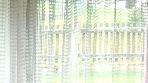 Weiße Gardinen hängen vor einem Fenster und lassen Licht herein, während ein Zaun im Hintergrund sichtbar ist.