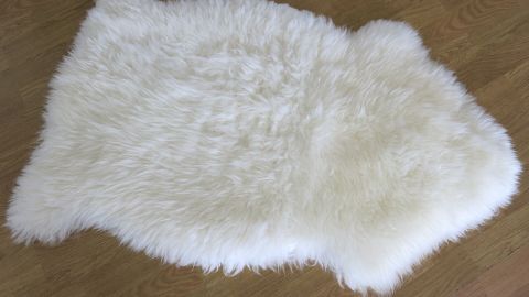 Lammfell wird wie neu mit einer Tierhaarbürste mit Drahtborsten aus dem Tierzubehörladen. Lammfell ist auch in der Maschine waschbar, mit Lammfellshampoo aus dem Babyladen. Ein weiches, weißes Lammfell liegt auf einem Holzboden und sieht frisch gereinigt und flauschig aus, bereit zur Nutzung.