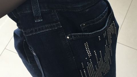 Eine Hand hält einen Föhn, der auf eine nasse Jeans gerichtet ist, während er sie in einem hellen Raum trocknet.