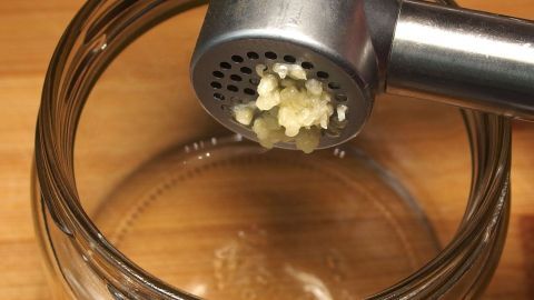Knoblauch im Glas: So hast du immer Knoblauch zum Würzen zur Hand. Eine Knoblauchpresse drückt frischen Knoblauch in ein Glas, bereit zur sofortigen Verwendung in der Küche.