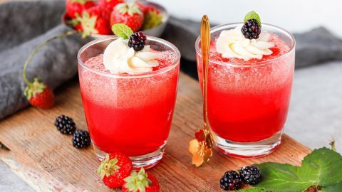 Zwei Gläser mit roter „Berliner Luft“-Nachspeise stehen auf einem rustikalen Holzbrett, dekoriert mit Beeren und Minze.