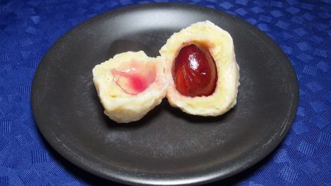 Zwei halbierte Zwetschgenknödel liegen auf einem schwarzen Teller, gefüllt mit einer saftigen Pflaume und roter Füllung.