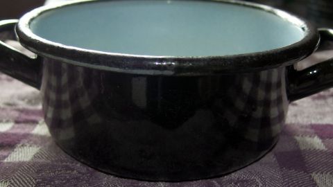Topf mit heißem Wasser als Ersatz für ein Bügeleisen verwenden. Ein Topf steht auf einem karierten Tisch, bereit, als Bügeleisenersatz zum Glätten von Kleidung verwendet zu werden.
