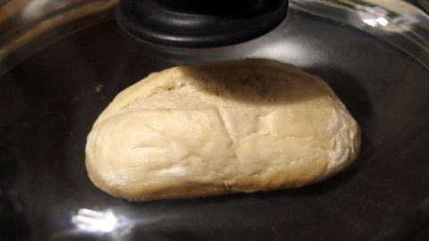 Energiesparendes Aufbacken von Brötchen in der Bratpfanne oder einem flachen Edelstahltopf. Ein Brötchen liegt auf einem Topf im Dampf, während es energiesparend aufbacken wird und eine goldene Farbe annimmt.