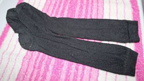 Schwarze Kniestrümpfe liegen ordentlich auf einem pink-weißen gestreiften Stoff, bereit, getragen zu werden.