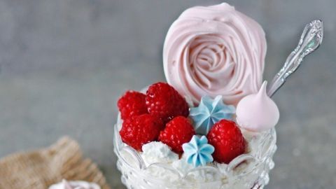 Eine köstliche Himbeertraumcreme in einem eleganten Glas mit Himbeeren, rosa Sahne und bunten Dekorationen auf einem rustikalen Tisch.