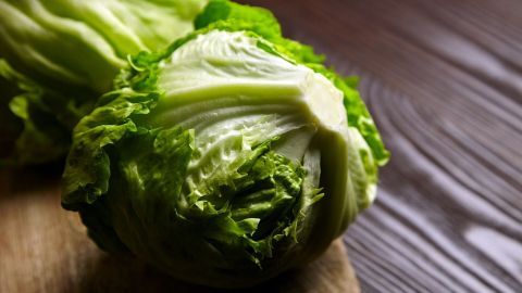 Ein frischer Eisbergsalat liegt auf einem Holzbrett und zeigt seine knackigen, grünen Blätter in natürlicher Beleuchtung.