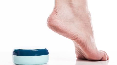 Eine Fußsohle steht auf einer weißen Oberfläche neben einer Dose Penatencreme, die zur Pflege bei Schweißfüßen verwendet wird.