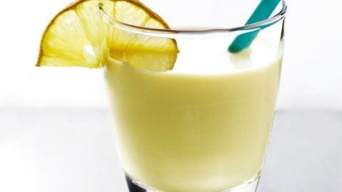 Ein Glas mit einer milchigen Flüssigkeit steht auf einer Oberfläche, garniert mit einer Zitronenscheibe und einem Strohhalm.