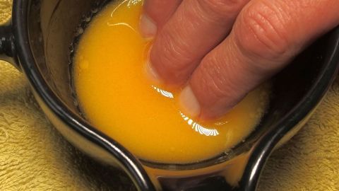 Eine Hand mit gepflegten Fingernägeln taucht in eine Schüssel mit frischem Ei, um die Nägel zu stärken und zu pflegen.