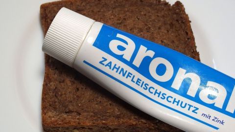 Ein Tipp zum Schmunzeln: Wenn man es morgens eilig hat - Frühstück und Zähneputzen in einem. Eine Zahnpasta-Tube liegt auf einer Scheibe Vollkornbrot, was das Zusammenbringen von Frühstück und Zähneputzen zeigt.