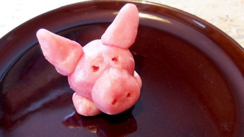 Ein rosafarbener Marzipan-Schweinchen steht auf einem dunklen Teller und vermittelt ein Gefühl von Glück und Freude.