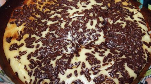 Ein cremiger Ofenquark mit Schokoladenstückchen ist goldbraun gebacken und auf einem Teller angerichtet, umgeben von buntem Geschirr.