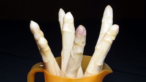 Frischer Spargel steht aufrecht in einem orangefarbenen Behälter, der auf einem dunklen Hintergrund positioniert ist.