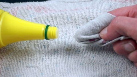 Flecken auf hellem Teppich? Diese kann man mithilfe von Zitronensaft entfernen. Ein gelbes Zitronensaftfläschchen wird über ein sauberes Tuch gehalten, während eine Hand das Tuch zum Entfernen von Teppichflecken benutzt.