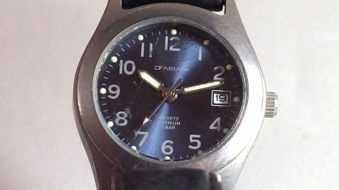 Eine Uhr mit Plexiglasglas liegt auf einer hellen Oberfläche, Kratzer sind sichtbar, was die Oberfläche beeinträchtigt.