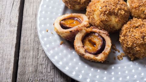 Runde, goldbraune Böhmische Zwetschgenknödel aus Quarkteig liegen auf einem weißen Teller, einige sind aufgeschnitten.
