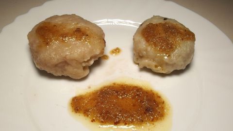 Zwei goldbraun gebratene Obstknödel aus Hefeteig liegen auf einem weißen Teller, umgeben von einer süßen Sauce.