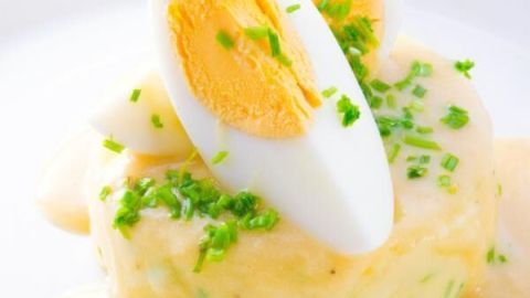 Gekochte Eier liegen auf einem Kartoffelpüree, dekoriert mit Schnittlauch und einer cremigen Sauce auf einem weißen Teller.