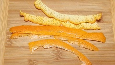 Dünne Streifen von Orangen- und Zitronenschale liegen auf einem Holzbrett und zeigen frische Aromen zum Kochen und Backen.