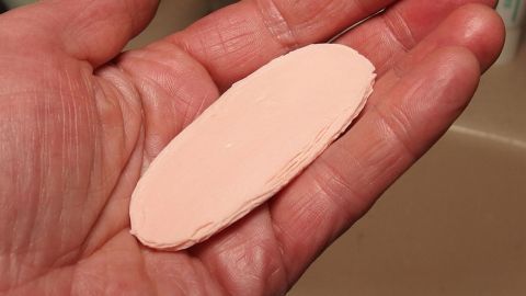 Eine Hand hält einen Seifenrest, der in einem Badezimmer mit hellen Oberflächen sichtbar ist, bereit zur Verwertung.