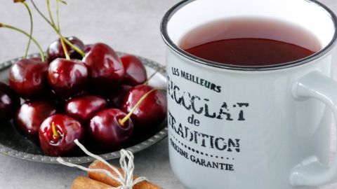 Heißer Kirschsaft ersetzt den Kinderpunsch und ist sehr angenehm in der kalten Jahreszeit! Es ist auch kein extra Zucker nötig wie bei Früchtetee. Ein Becher mit heißem Kirschsaft steht neben frischen Kirschen und Zimtsticks auf einer Tischoberfläche.
