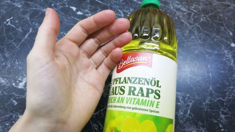 Eine Hand hält eine Flasche Rapsöl, um Geräte und Hände nach dem Schälen von Schwarzwurzel zu reinigen.